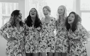 A group of bridesmaids in matching floral dresses share a candid laughing moment together.