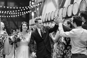 Wedding party celebrates with high fives in a barrel room decorated with string lights.
