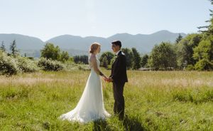 A wedding couple stands in a scenic mountain meadow with rolling hills in the background.