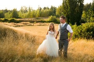 A couple walks through a sun-drenched field with mountains and forest in the background.