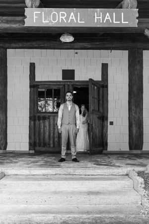 Black and white photo of two people standing in front of a rustic entrance marked Floral Hall.