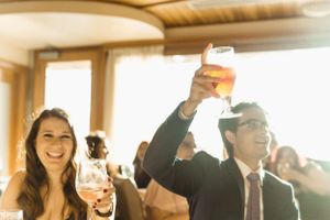 Wedding celebration guests raise glasses in a toast during a sun-lit reception.