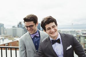 Two people in formal attire share a laugh on a rooftop with city views.