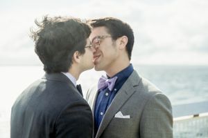 Two people share an intimate kiss against a bright oceanside backdrop.