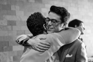 Two people embrace warmly in front of a brick wall in black and white.