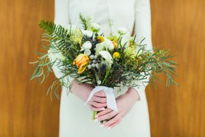 Close-up of hands holding a delicate bouquet with ferns and yellow flowers.