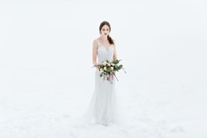 Person in flowing white dress holds bouquet against winter white backdrop.