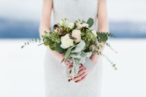 Close-up of bridal bouquet with white roses and eucalyptus against snowy backdrop.