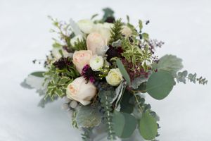 A romantic wedding bouquet with white roses, eucalyptus leaves, and burgundy accents arranged naturally on a light background.