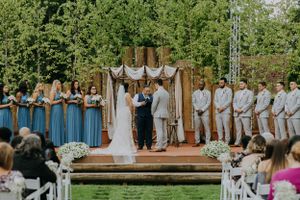 Outdoor wedding ceremony with blue bridesmaid dresses and rustic wooden arch decoration.