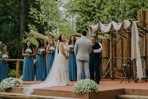 Wedding ceremony on elevated wooden platform with blue bridesmaids and floral arrangements.
