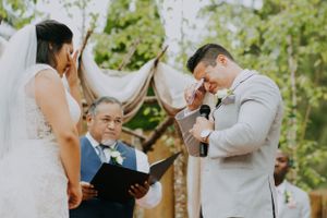 Emotional wedding ceremony moment under rustic wooden arch in garden setting.
