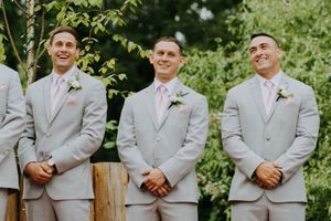 Groomsmen in light gray suits with boutonnieres smiling outdoors.