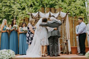 Wedding ceremony moment under draped fabric arch with wedding party in blue and gray attire.