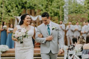 Newlyweds walking down the aisle at outdoor garden ceremony with guests in background.
