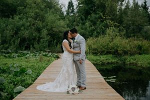 A couple shares a romantic moment on a wooden dock surrounded by lush greenery and water.
