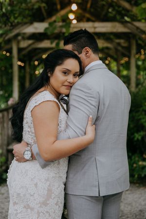 A tender moment between newlyweds in a garden setting with twinkling lights overhead.