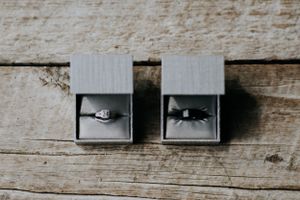 Two gray jewelry boxes containing wedding rings displayed on weathered wooden surface.