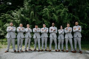 Wedding party members in coordinated gray suits stand in line against pine trees.