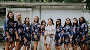 Bridal party in matching navy floral robes poses together on outdoor porch.
