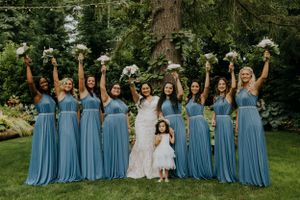 Bridesmaids in blue dresses hold bouquets while posing with the bride in a garden setting.