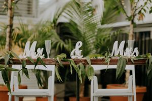 White 'Mr & Mrs' text decorations on chairs with tropical greenery.