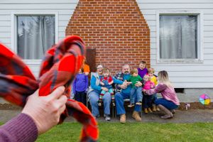 Multiple people sit together on a bench in front of a brick chimney at a residential home.