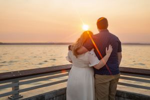 A couple embraces on a pier while watching a vibrant sunset over the water.
