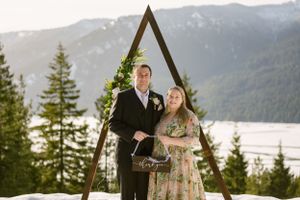 A couple poses under a triangular arch frame with snow-capped mountains in the background.