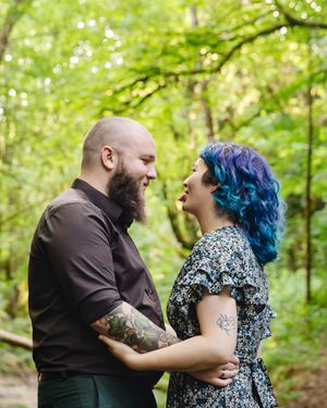 A couple shares an intimate moment together in a lush green forest setting.