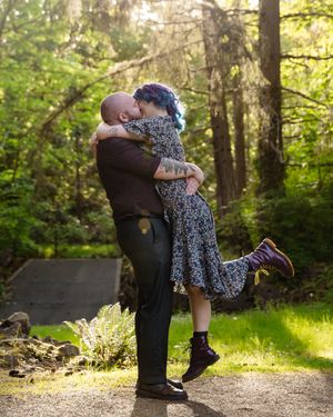 A romantic moment captured in a forest as a couple embraces on a sunlit path.