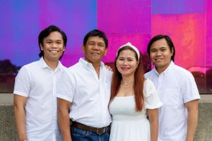 Family group in coordinated white outfits poses together against vibrant colorful backdrop.