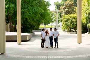Group in white attire stands together under covered walkway surrounded by greenery.