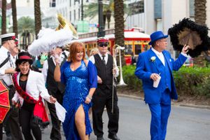 Lively Second Line parade with performers in bright costumes marching along a palm-lined street in New Orleans.
