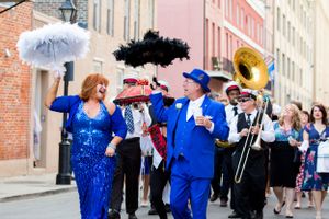 Street performers with parasols and brass instruments leading a festive parade through city streets.