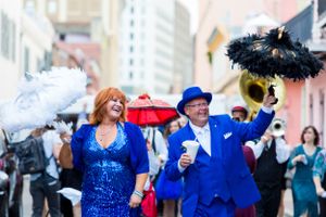 Joyful parade performers in matching blue outfits dancing with decorative parasols amid an urban setting.