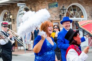 Festive parade performers with decorative parasols entertaining crowds in front of historic architecture.