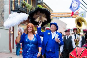 Second line parade performers with black and white parasols marching alongside brass band musicians.