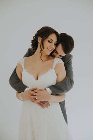 Intimate embrace between couple in wedding attire against white backdrop.