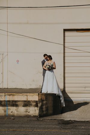 Wedding couple poses against industrial white wall with dramatic shadows.