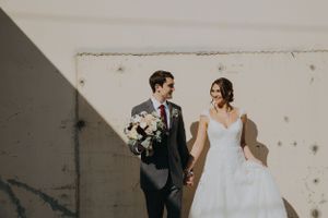 Romantic portrait of couple in wedding attire against white wall with natural lighting.