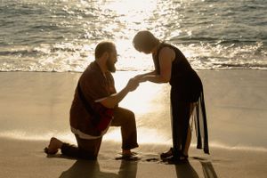 A beachside proposal during golden hour with boats in the distance.