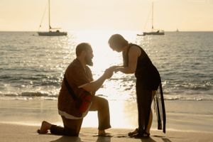 A sunset proposal scene on the beach with sailboats floating in the background.