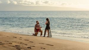 A special moment unfolds on a beach with sailboats in the distance during golden hour.