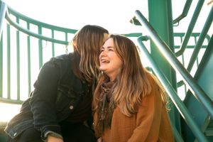 Two people laugh together on a green metal structure in warm sunlight.