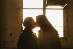 Silhouetted couple sharing an intimate moment in front of a sunlit window.