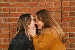 Intimate couple portrait against rustic brick wall in warm lighting.
