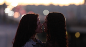 Silhouette of two people with long hair in intimate moment at dusk.