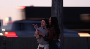 Two figures point towards the horizon during twilight in an urban setting.