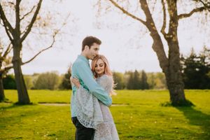 A tender embrace shared in a sunlit park with blooming spring trees in the background.